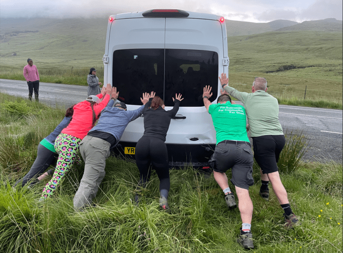 group of hikers pushing a minibus back onto the road